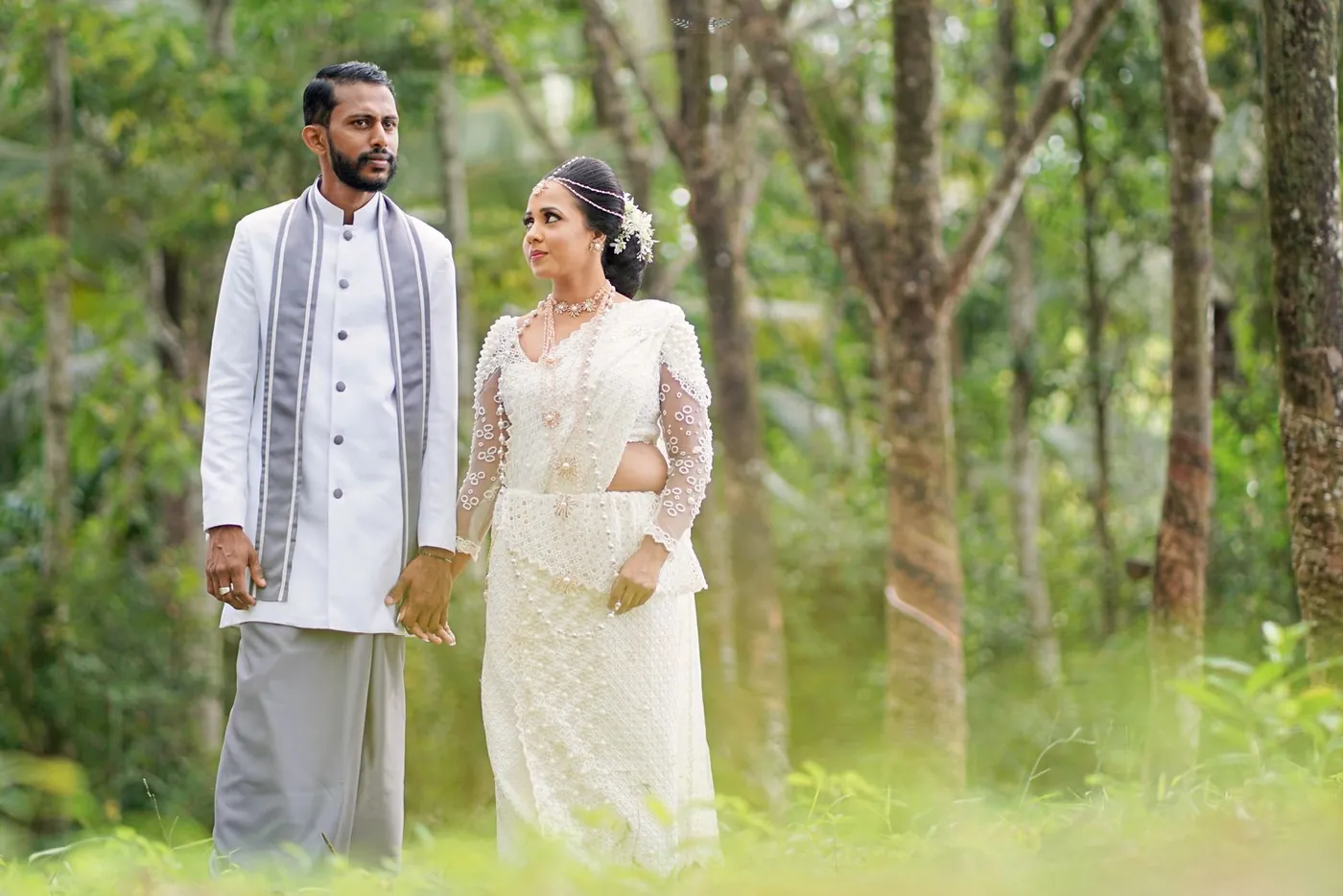A Sri Lankan couple in traditional wedding dress, holding hands in a forest
